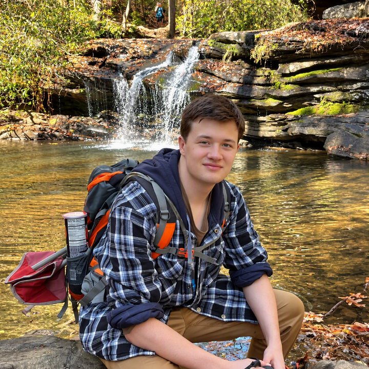 Gabriel sitting on a rock by a creek, in front of a waterfall