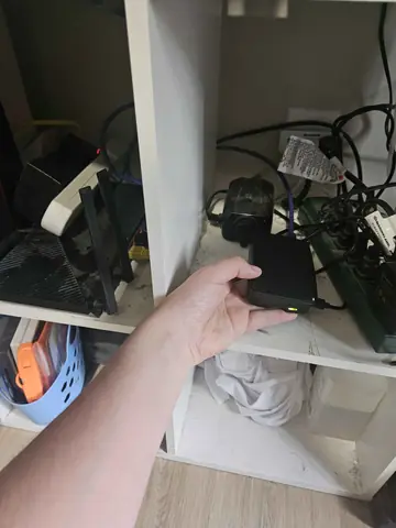 A hand holding the Raspberry Pi 5 in its case, on a shelf beside the router